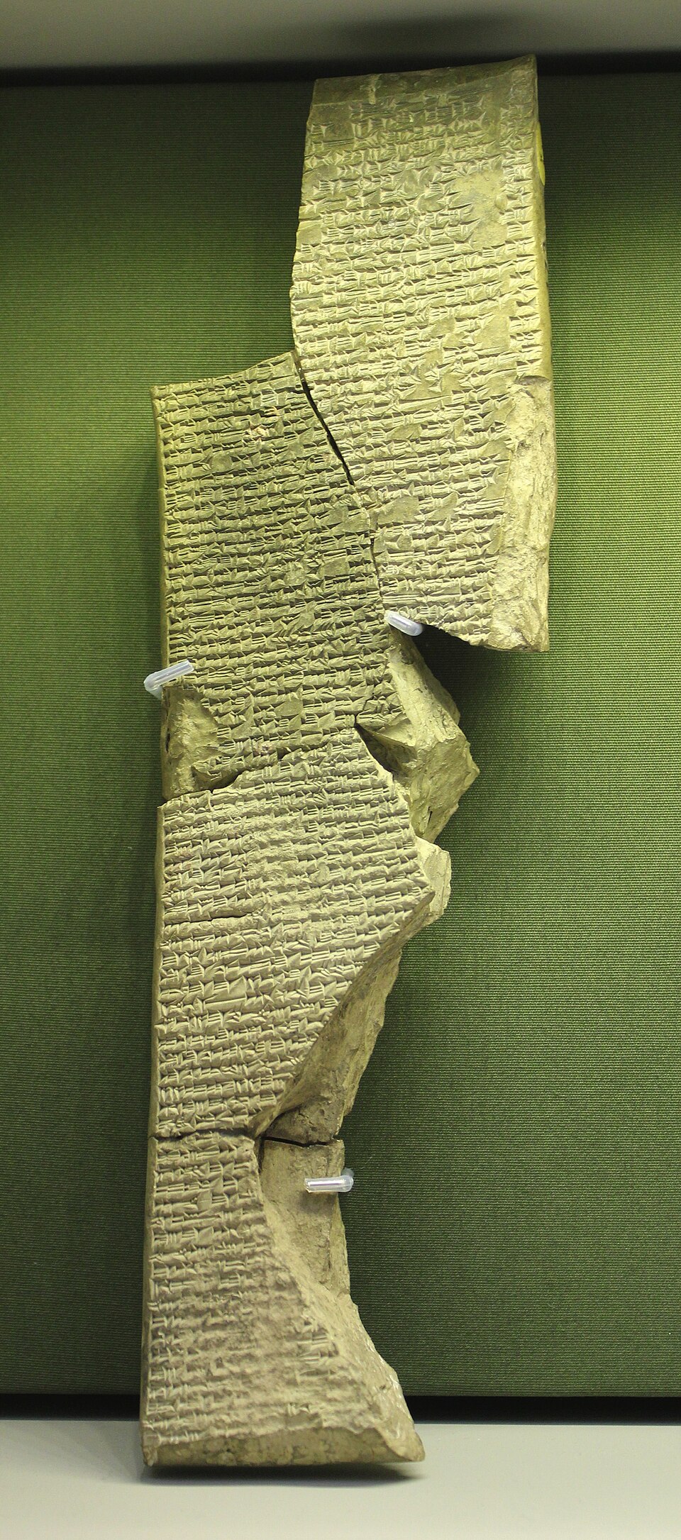 Varios fragmentos unidos de una tablilla vertical de arcilla con numerosas líneas de escritura cuneiforme.